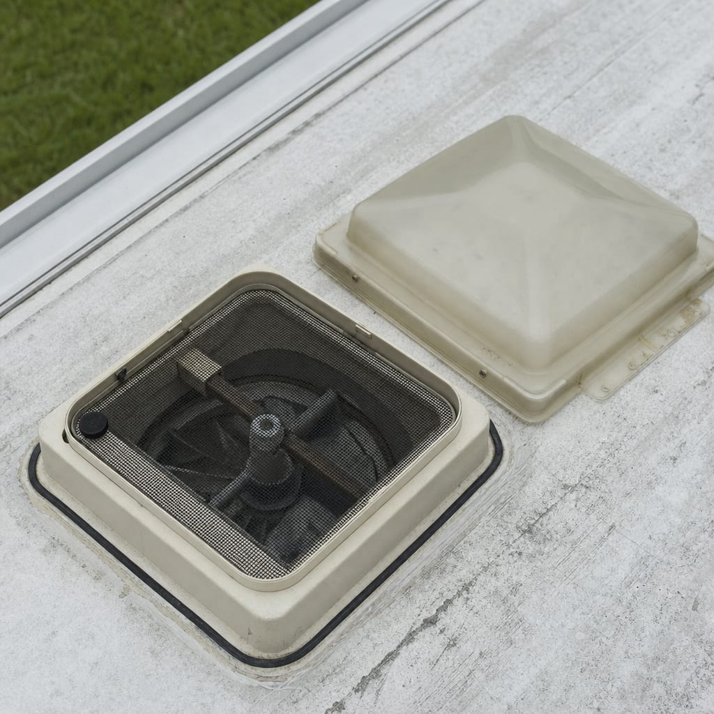 RV roof vent with the plastic lid detached, exposing the screened opening and mounting base in daylight